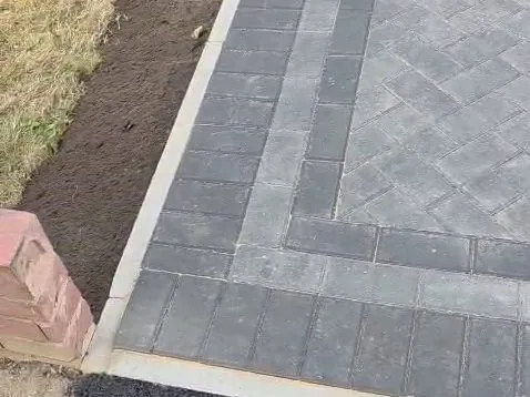 Close-up of charcoal herringbone block paving with double soldier-course border against fresh topsoil