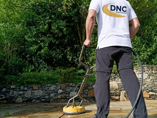 A DNC Block Paving fitter pressure washing a stone patio with a rotary surface cleaner
