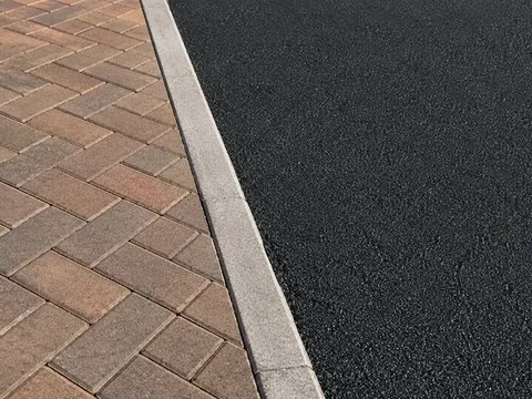 Concrete kerb running between fresh black tarmac and brindle block paving