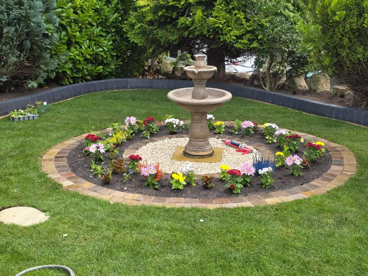Round planted bed edged with two courses of block paving, a two-tier stone fountain at its centre and new lawn all around it