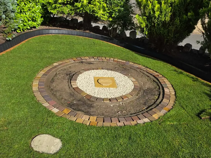 A finished circular bed seen from above, edged with two courses of block paving around a gravel centre, with new turf all around it