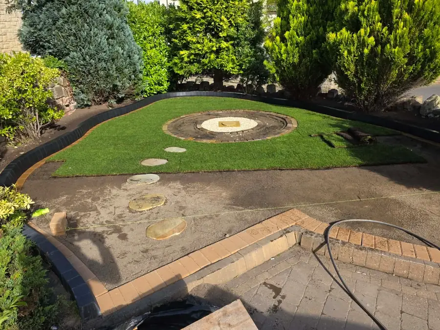 Fresh turf laid around a shaped bed with a central stone base and round stepping stones