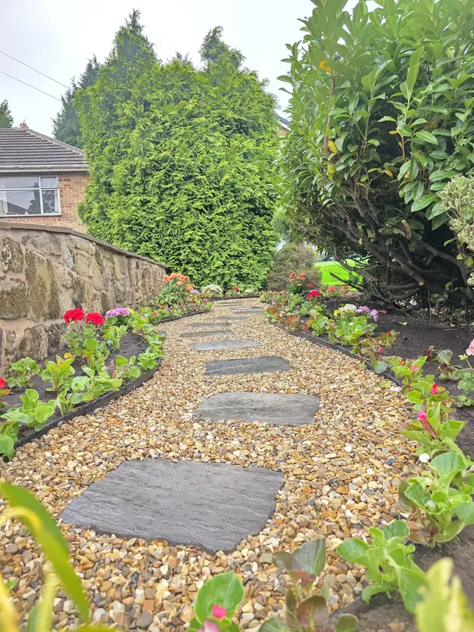 Finished gravel path with dark stepping stones and flowers planted along both sides