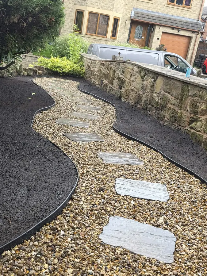A curved gravel path with large stepping stones, edged with darker gravel beside a stone wall