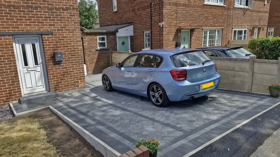 The back of a light blue car parked on the herringbone drive, with the front door on the left and the charcoal double border running along the lawn
